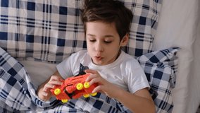 little boy lies in bed covered with a blanket and plays with his orange plastic robot. child has recovered from the illness and is in a good mood - Powered by Shutterstock - Get 15% off with code: PIKWIZARD15