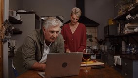 Caucasian elderly couple cooking in kitchen using laptop