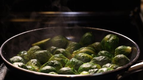 Steam coming from hot brussels sprouts while cooking in a pan. Vegan cooking, close up, dark mood shot.