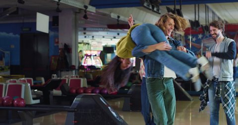 Cinematic shot of happy young arab female bowler throwing strike ball and exulting victory while having fun to play bowling together with multiracial college friends on weekend in sporting club.