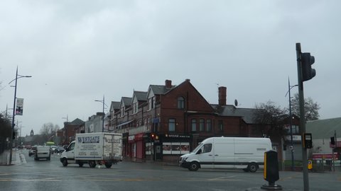 SALFORD, GREATER MANCHESTER, ENGLAND, UNITED KINGDOM - CIRCA FEBRUARY, 2022: Massage parlour and beauty salon on the corner of crossroads or intersection. Car windscreen view on a rainy day.