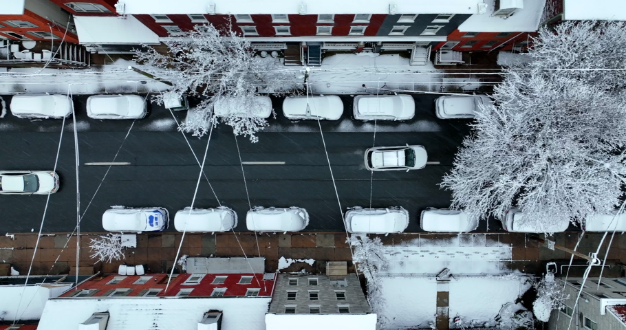 Tracking cars driving on two lane city street. Fresh snow coats trees in urban town in USA. Residential housing and sidewalks. Aerial truck shot.