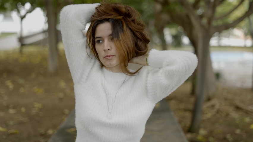 Young flirty woman in park touches hair and kisses toward camera