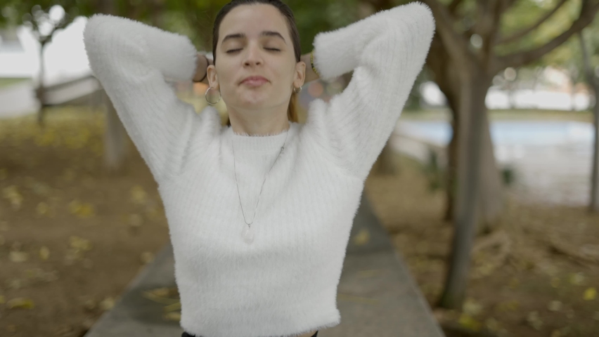 Young pretty woman in park with eyes shut fixes her hair, close slomo