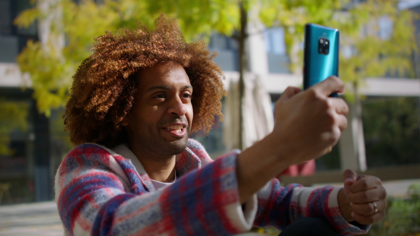 Cool multiracial mid audlt man having video call with smartphone outdoors in town