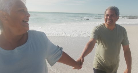 Happy hispanic senior couple walking on beach at sunset. love, romance and active retirement lifestyle.