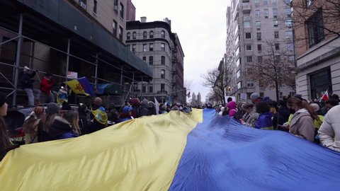 New York, New York USA - 02.24.2022 Protesting March against war in Ukraine started by Russia. Ukrainian protesters stretched a large Ukrainian flag near Russian embassy slow motion