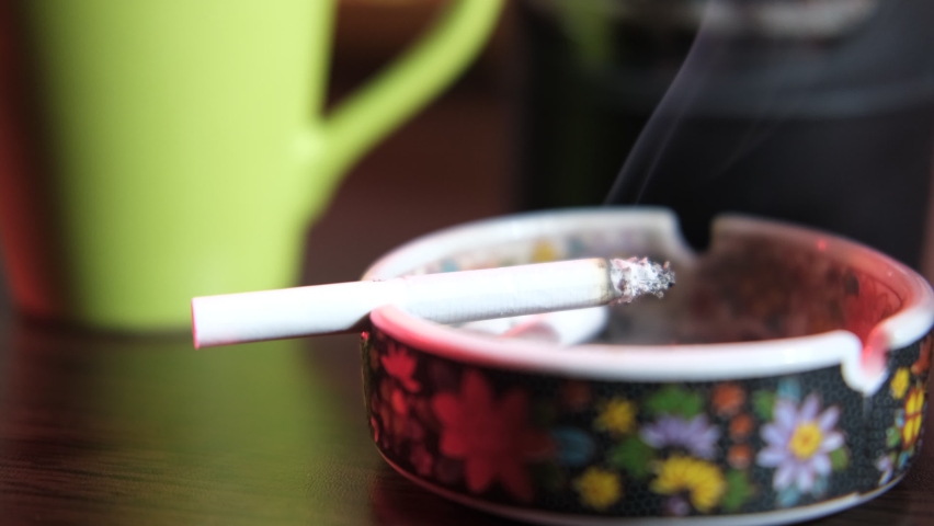 Close-up view of coffee and cigarette ashtray, coffee and cigarette smoke pairing | Shutterstock HD Video #1087553084