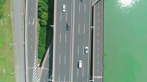 Aerial top down tilt view of a highway overpass multilevel junction with fast moving cars surrounded by green trees and with a river on a side on a sunny day.