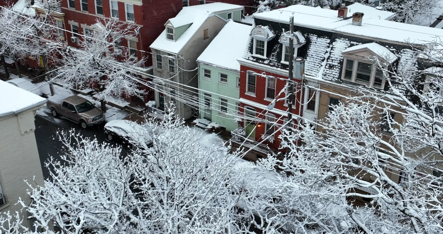 Aerial pan reveals homes in USA during winter snow. Trees coated in snowy scene.