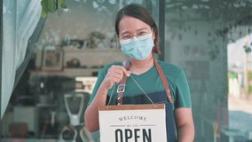 female cafe owner holds up a sign to show she is open for business.Asian woman with mask business owner opening store. - Powered by Shutterstock - Get 15% off with code: PIKWIZARD15