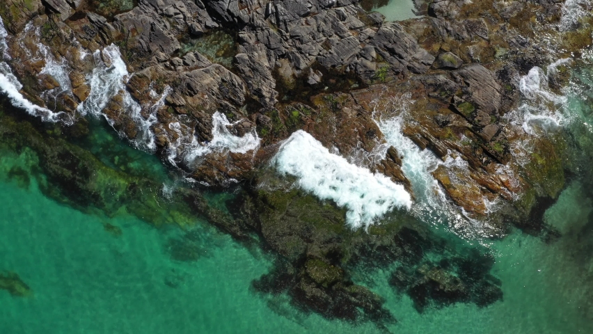 Top down View on the Rocky Beach with Splashing Sea Waves.Aerial view of a transparent blue sea with beautiful waves at the sunny day . | Shutterstock HD Video #1087560431