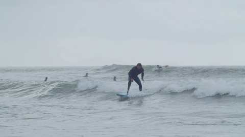 Fit man with artificial leg surfing in ocean. Long shot of focused sportsman in wetsuit riding wave on surfboard, practicing surfing skills, spending time outdoor. Disability, extreme sport concept