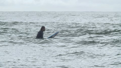Focused sportsman with disability surfing in ocean. Long shot of man with artificial leg having workout in morning, waiting for wave, lying on surfboard. Disability, extreme sport concept