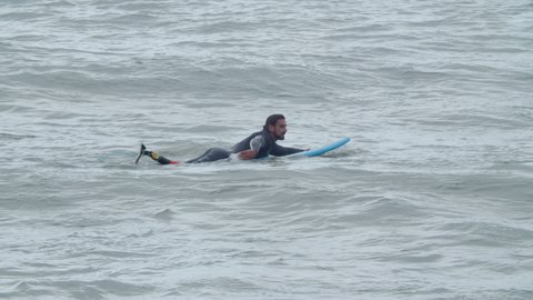 Focused surfer with artificial leg swimming on surfboard. Long shot of sportsman in wetsuit training alone, waiting for wave to ride, spending time outdoor. Disability, extreme sport concept