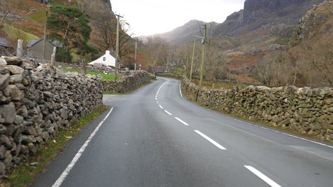 Driving framed with stone wall fence winding A4086 road from Llanberis in Snowdonia mountains through small Welsh village in autumn.