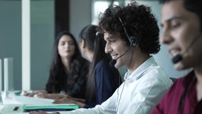 Beautiful young indian man customer service on headphone, working, smiling, talking, pleased to service, among blurry bacground of coleagues.4 pepople call center business concept. - Powered by Shutterstock - Get 15% off with code: PIKWIZARD15
