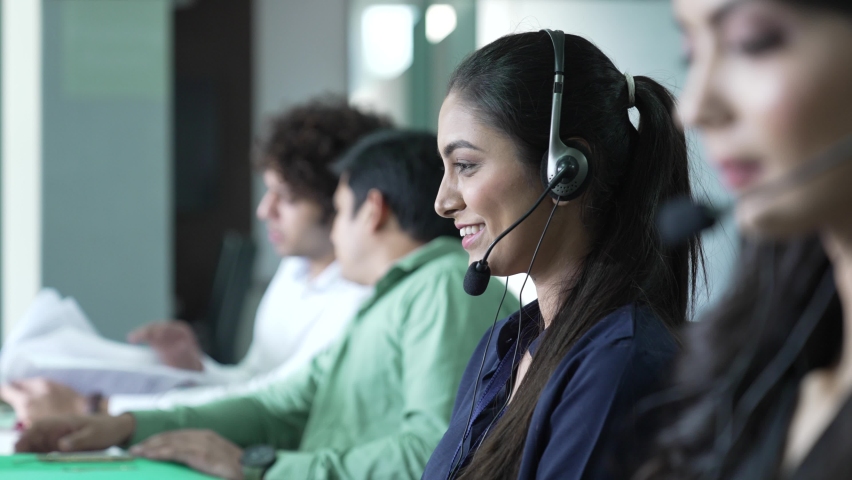 Diverse group of indian woman employees are making calls using headsets and laptops working in call center busy with communication and customer support. Indian man look at camera and smiling. - Powered by Shutterstock - Get 15% off with code: PIKWIZARD15