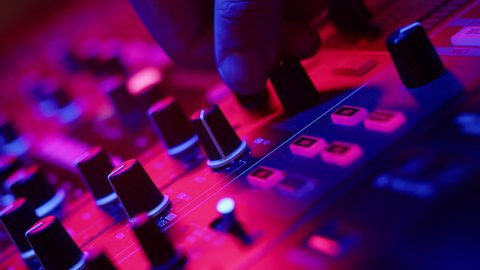 Closeup of DJs hands twisting knobs on mixing console adjusting volume of dubstep in nightclub disco club. DJ sets up hip hop music