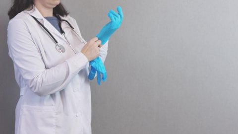 unrecognizable female doctor in white uniform, stethoscope around neck, putting on blue latex gloves protecting hands before work. woman physician preparing visit patient. medical occupation concept