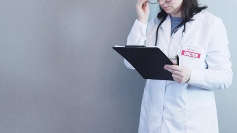 female doctor in white uniform, stethoscope around neck, black clipboard, pen in hand, taking off glasses, putting in pocket. unrecognizable caucasian woman physician end up work concept