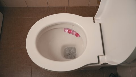 Ceramic toilet during a flush, close-up from above. Cleaning the toilet with foam. Home toilet with a pink smell block.