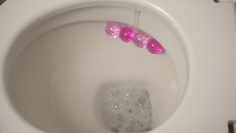 Ceramic toilet during a flush, close-up from above. Cleaning the toilet with foam. Home toilet with a pink smell block.
