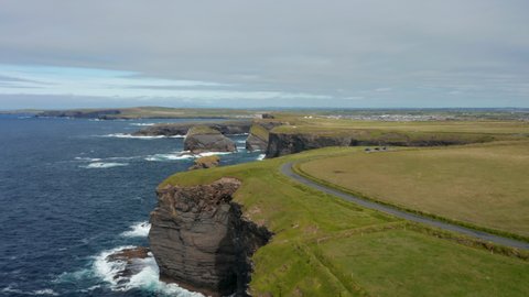 Fly above meadow above high cliffs steeply falling to sea surface. Aerial panoramic footage of natural landmark. Kilkee Cliff Walk, Ireland