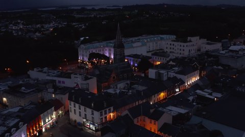 Fly above town development in evening. Aerial footage of historic city centre. Old church with tall tower and large building of luxury hotel. Killarney, Ireland