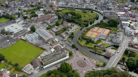 High angle view of tennis courts and large roundabout on river waterfront. Tilt up reveal of panoramic view of town. Ennis, Ireland