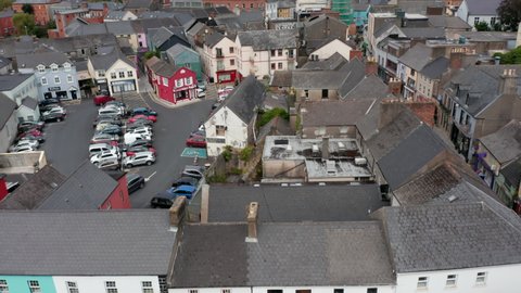 Fly above houses in urban borough. Square with parked cars around and in middle. Tilt up reveal of overcast sky. Ennis, Ireland