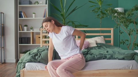 Young Woman Feels Back Pain on the Bed at Home, Rubs Her Lower Back, Trying To Relieve Muscle Tension. Uncomfortable Bed or Mattress, Poor Sleep, Stiffness in Movement, Worsening of Chronic Back Pain.