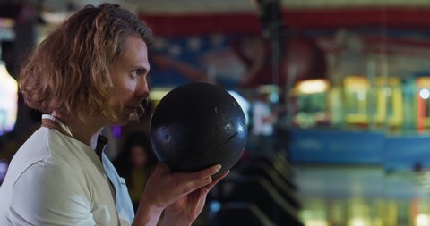 Cinematic close up of concentrated and determined young blond hair male bowler throwing strike ball and exulting victory while participates in bowling tournament competition in sporting club.