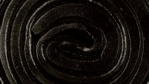 Extreme macro view with rotation of a licorice gummy candy spiral shaped. Dark chewy sweets. Candy texture pattern close up.