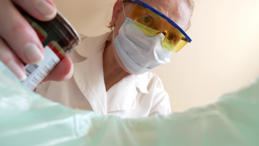 Woman doctor in medical respirator with hight protection throwing used medical trash in bin away, trash bin with pills, medical mask, galsses inside, medecine in trashcan