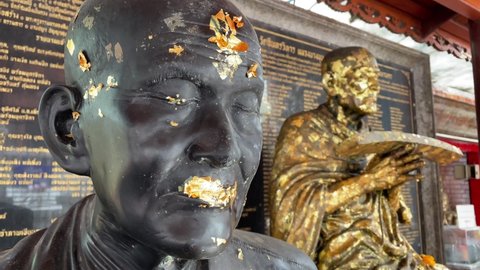 BANGKOK, THAILAND - NOVEMBER 15, 2021: Gilding buddha statues with gold leaf for good merit and enlightenment in a buddhist temple - Close up shot with blowing wind