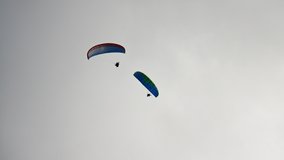 People try paragliding adventure sports flying with colorful parachutes against heavy white cumulus clouds on blue sky on autumn day, 4K video