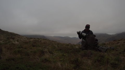 A photographer packing away a big camera lens in dark gloomy mountain landscape