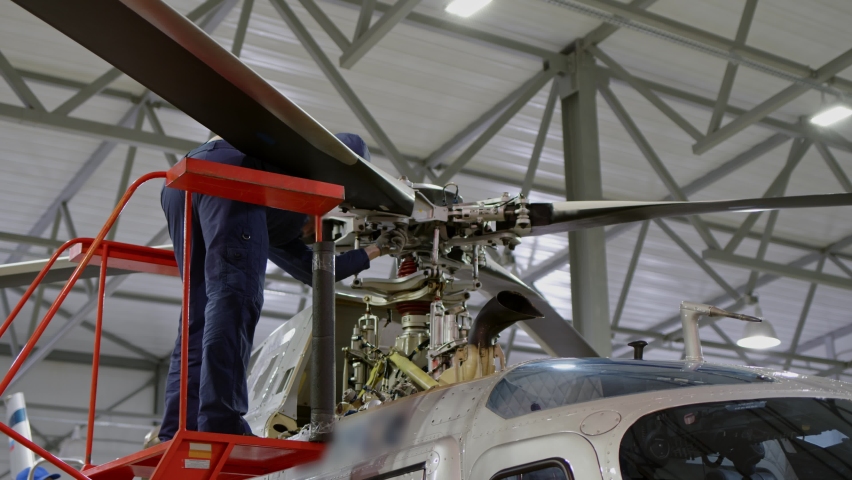 unrecognizable mechanic is turning nut on helicopter propeller. Large helicopter that is in hangar for repair and rebuild, on which blades are about to be removed, maintenance of air vehicle.