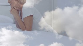 Animation of caucasian senior woman praying over moving clouds. religion, faith and christianity concept digitally generated video.