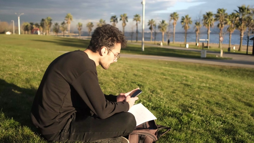 Image of young man spending time with his phone on the grass, having fun on the grass, summer in relaxtation on the grass