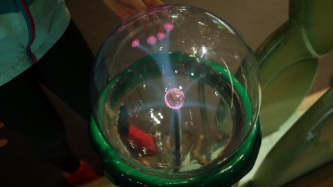 A girl puts fingers onto a plasma ball emitting electrical charge
