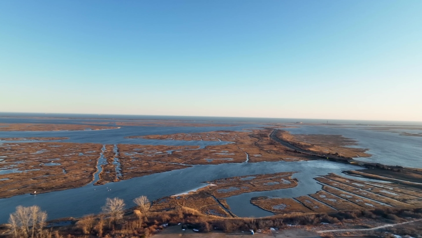 A high angle view of a brown salt marsh on Long Island, NY on a sunny day. The drone camera pan right high over the dry grass and water paths and reveal many solar panels.