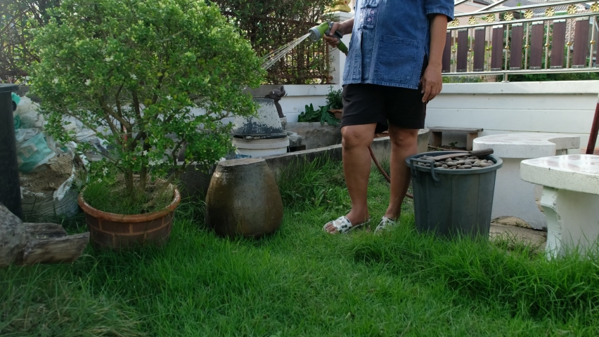 In a spring or summer time people are seeding planting or watering there home gardens. A women  is cutting and take care her flowers at house.