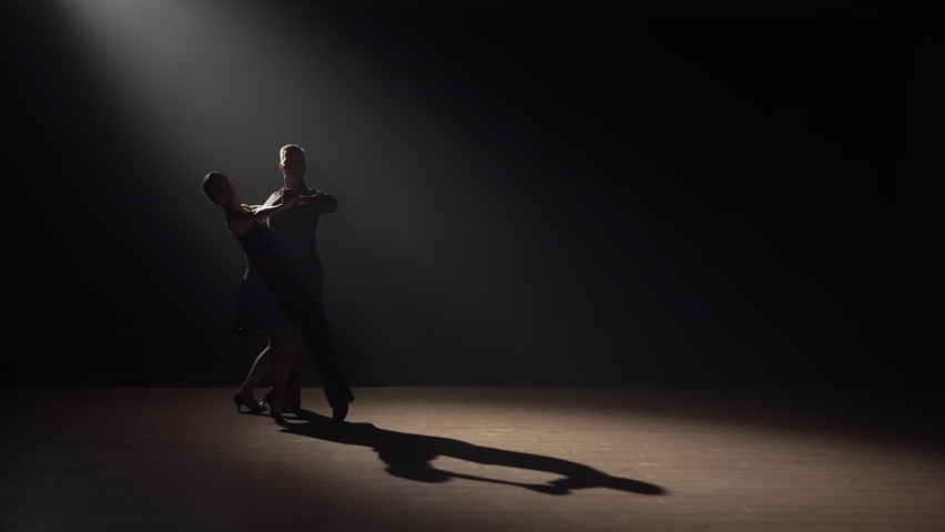 Silhouette of couple dancers dance tango in dark with smoke and spotlights. Pair of ballroom dancers. Choreography lesson at school of Latin American dances. Slow motion ready, 4K at 59.94fps. Royalty-Free Stock Footage #1087610732