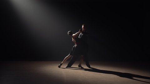 Silhouette of couple dancers dance tango in dark with smoke and spotlights. Pair of ballroom dancers. Choreography lesson at school of Latin American dances. Slow motion ready, 4K at 59.94fps.