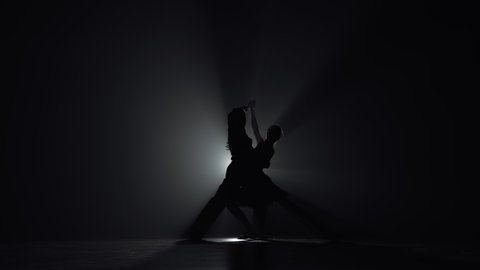 Elements of passionate Argentine tango performed by pair of dancers. Silhouettes of man and woman dancing latin dance choreography in dark with backlight and smoke. Slow motion ready, 4K at 59.94fps.