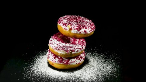 Donuts luxury, with pink chocolate, hazelnuts, sprinkled with powdered sugar. Dessert melts in the mouth. Gentle curd cream filling. Trendy dessert, directly above, black stone background.