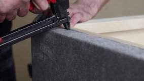Worker fixes the fabric with a pneumatic stapler and cuts off excess upholstery with a knife in the factory shop. Manufacture of upholstered cabinet furniture. Slow motion 4k video