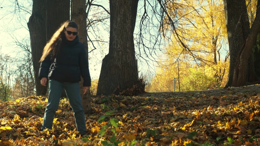 a girl kicks fallen leaves in the park. then he runs away looking back at the camera. autumn park. a frenzied mood